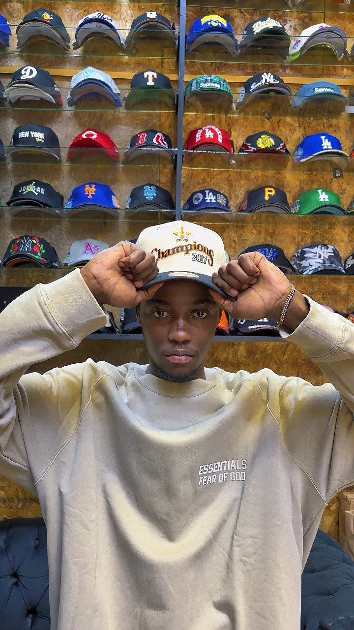 Young man wearing a white Champions baseball cap and beige sweatshirt in a hat store.