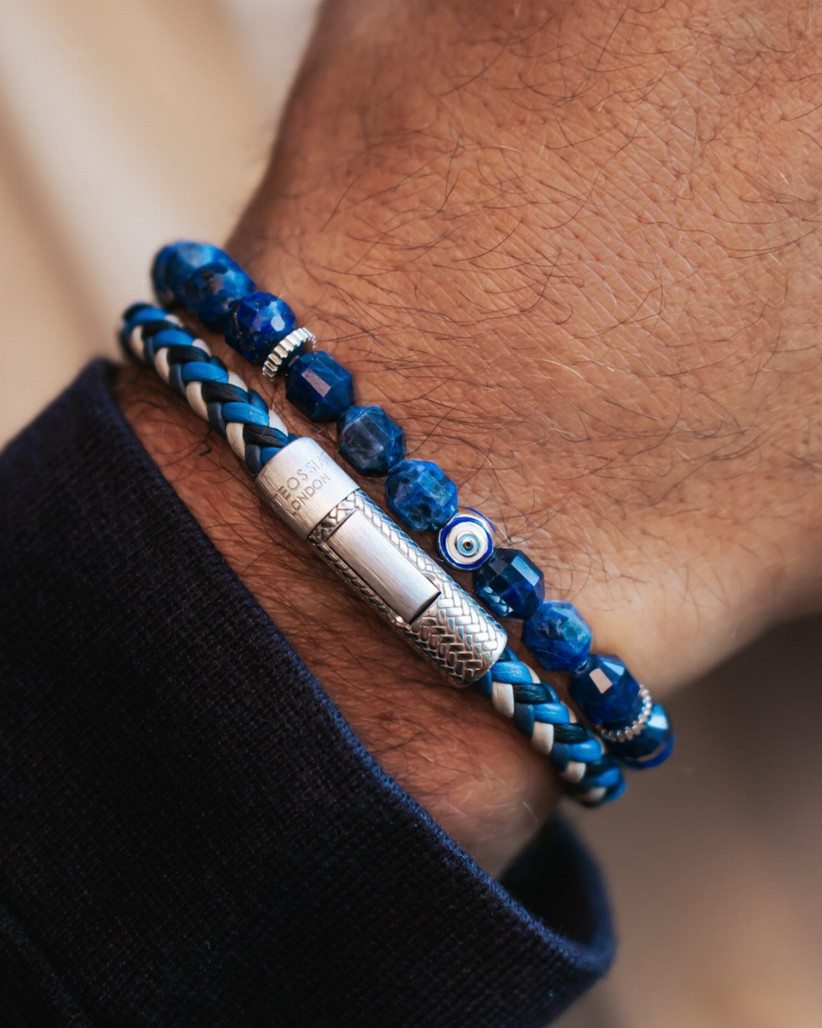 Blue beaded and braided leather bracelets on a man's wrist with a blue sleeve.