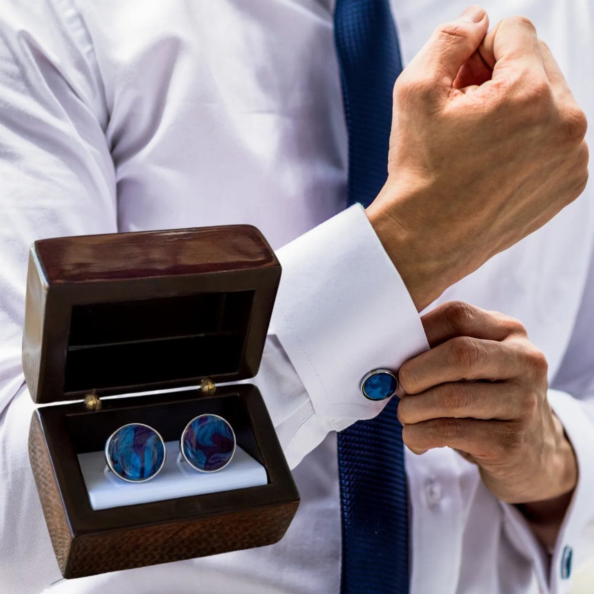 Man fastening blue marbled cufflinks to a white dress shirt sleeve.