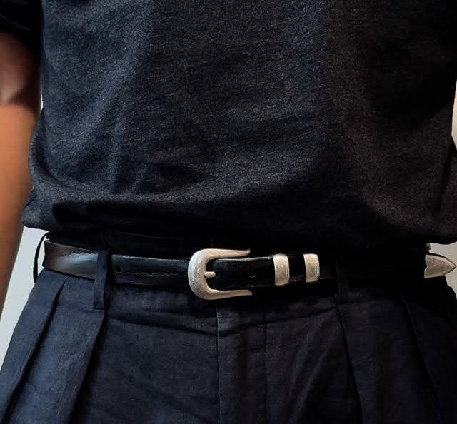 Black leather belt with silver buckle worn with black t-shirt and pleated trousers.