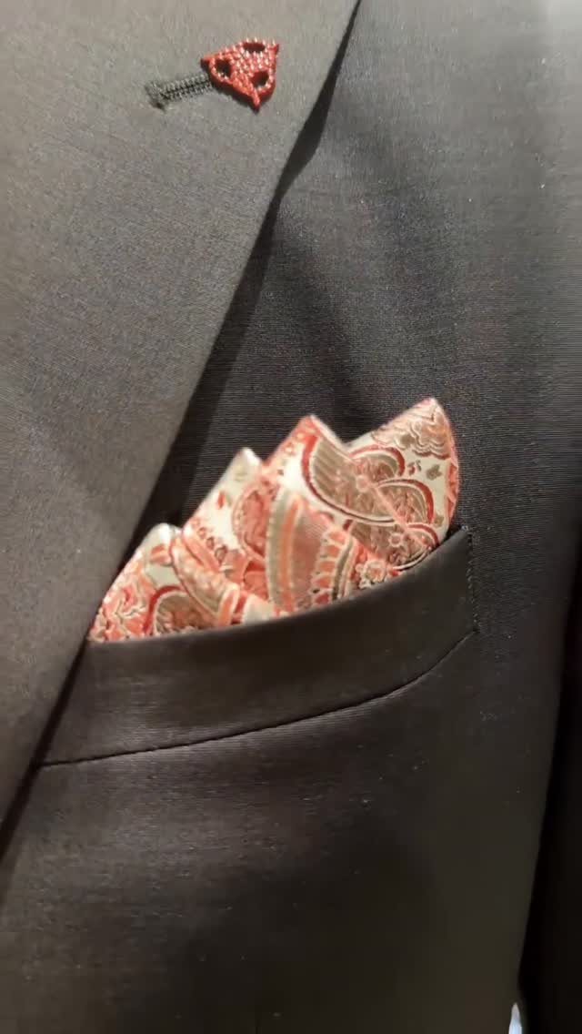 Red paisley pocket square and red lapel pin on a dark grey suit jacket.