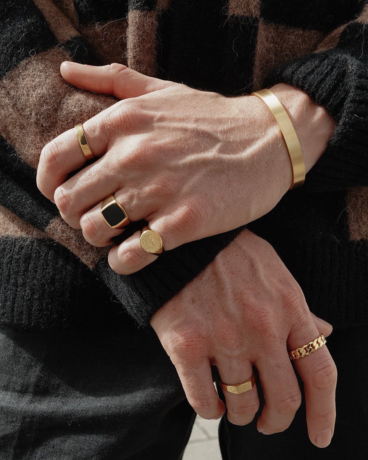 Gold rings and a gold cuff bracelet worn on a person's hands.