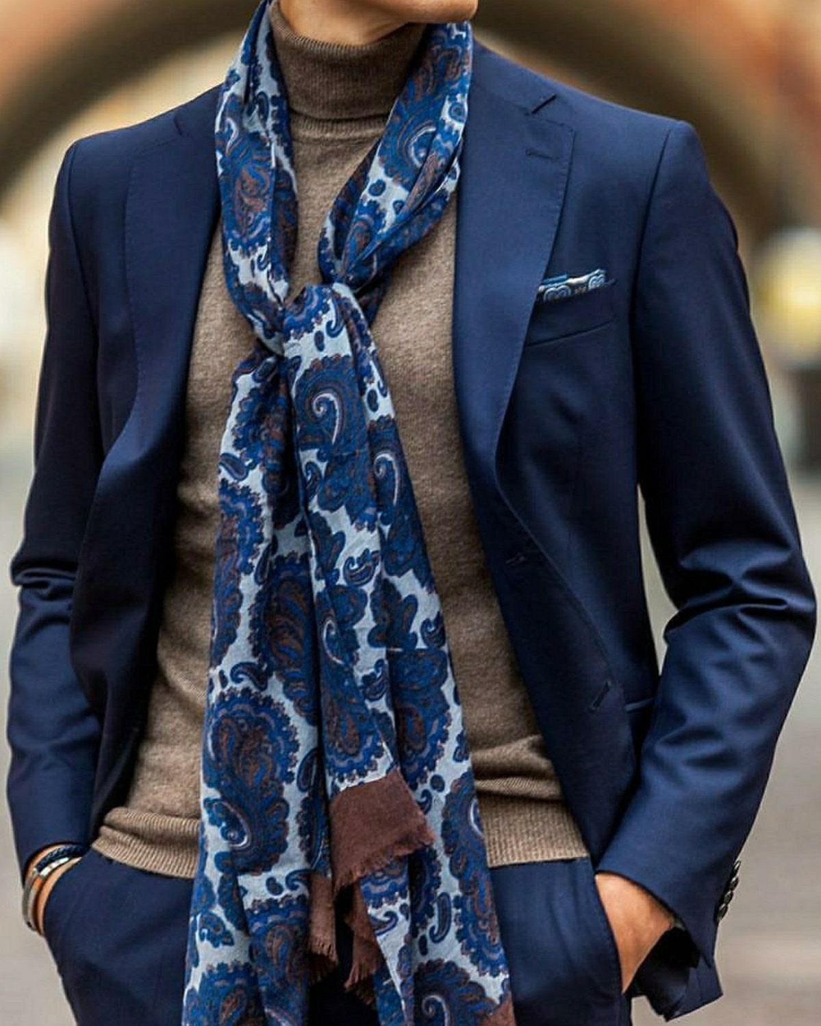 Man in a navy suit and brown turtleneck wearing a blue paisley scarf.