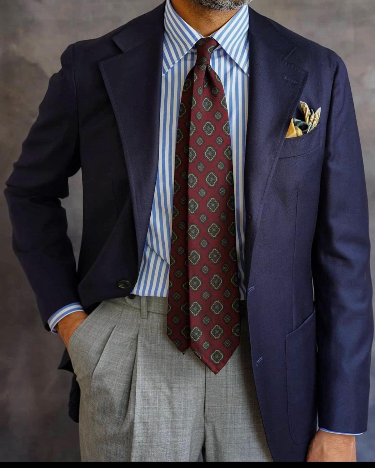 Man wearing a navy blazer, striped shirt, and a burgundy patterned necktie.
