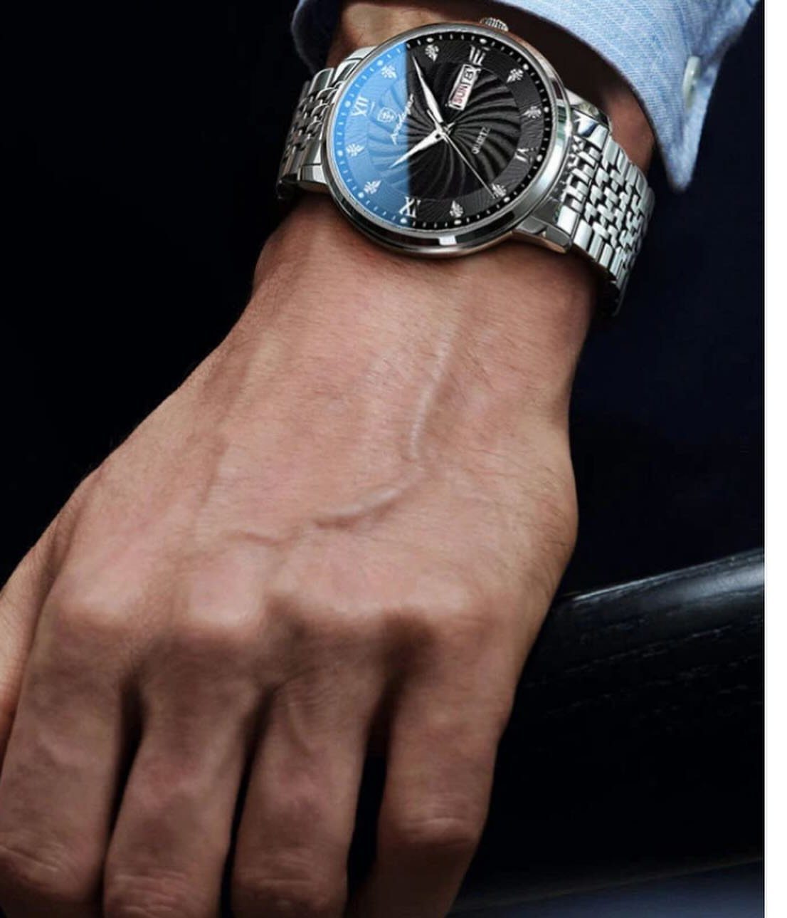 Silver wristwatch with blue dial on a man's wrist wearing a suit jacket.
