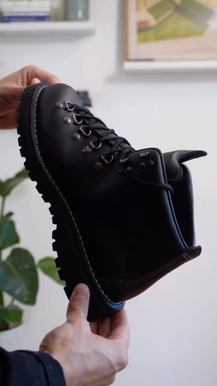Black leather lace-up boot with thick lug sole held by two hands.