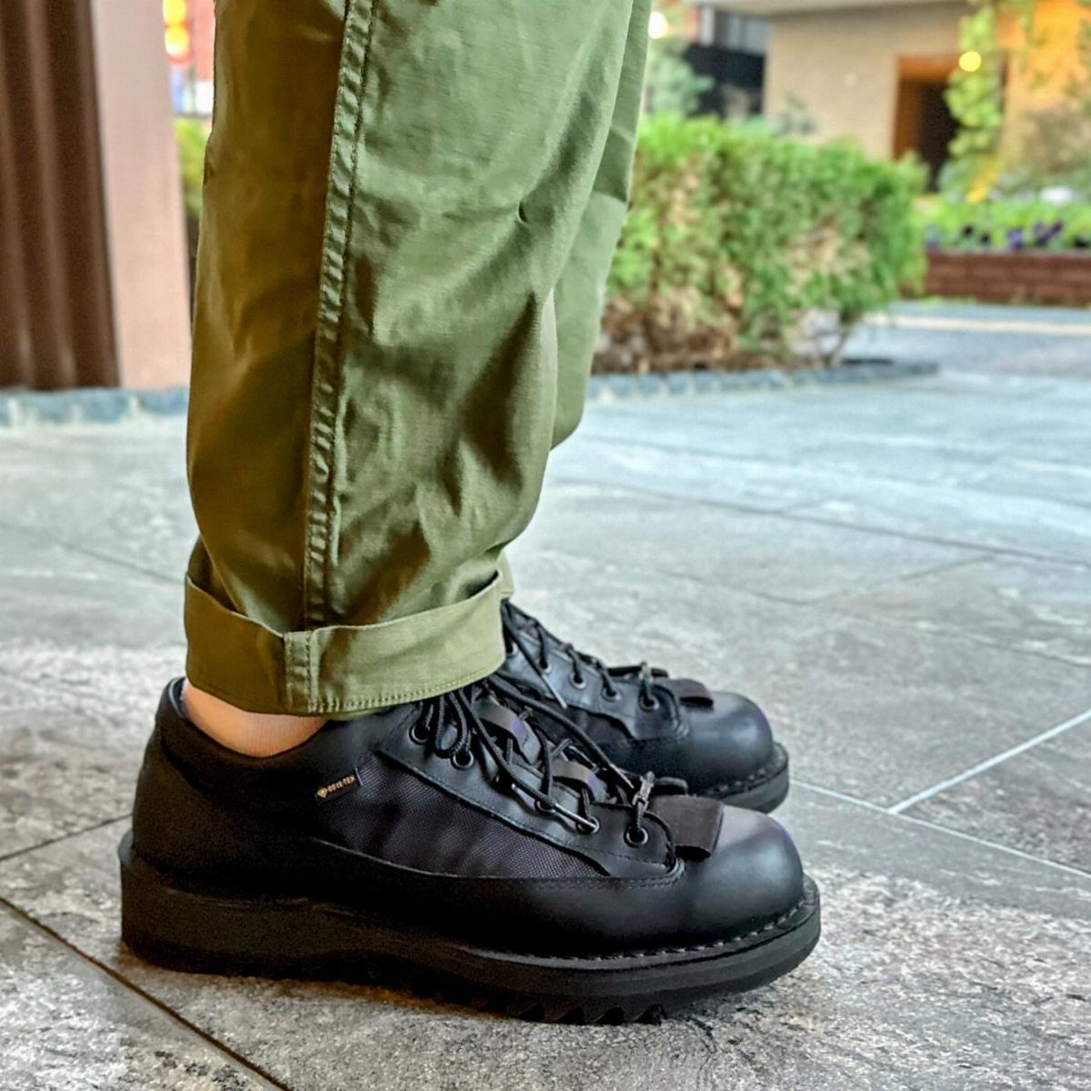 Black leather and nylon hiking boots worn with olive green rolled-up trousers.