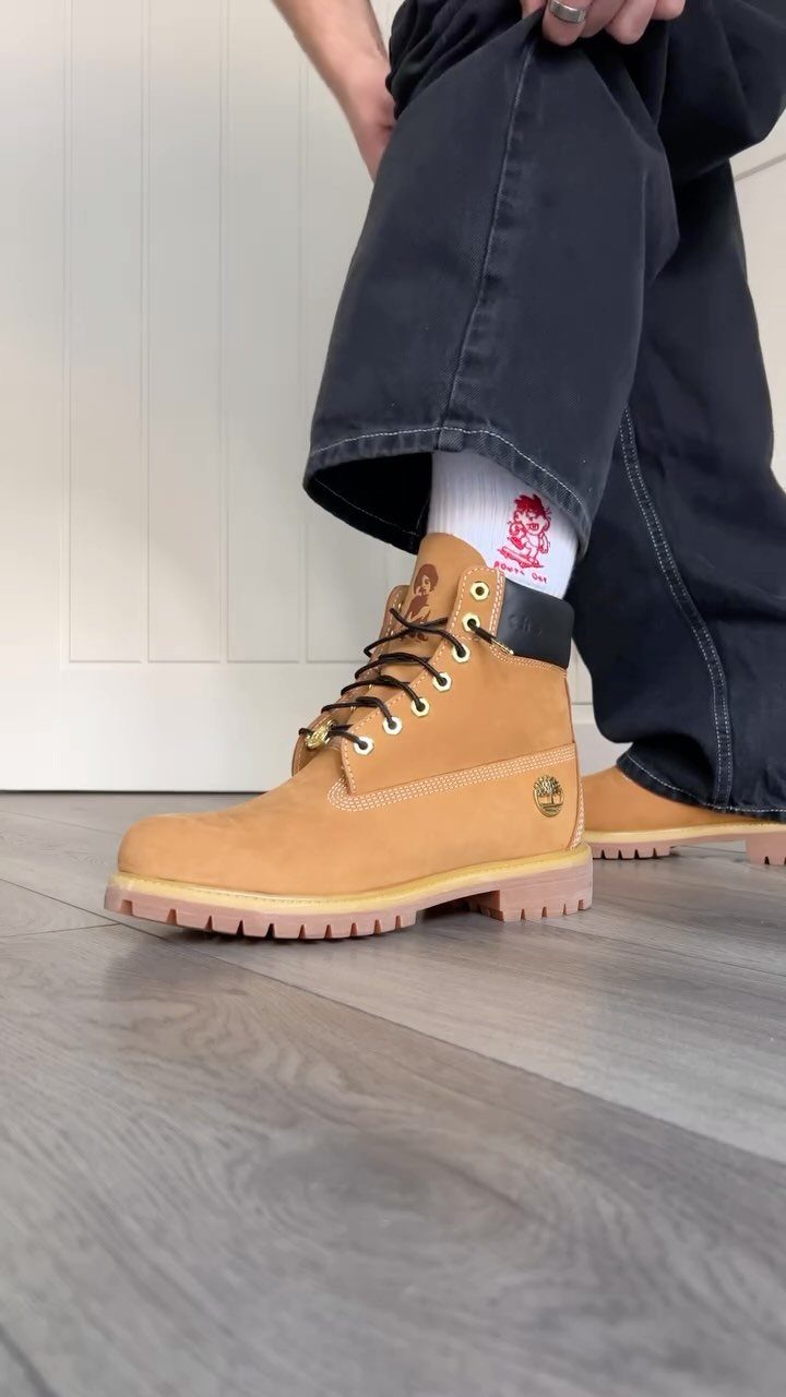 Tan leather work boots worn with black trousers on a grey wooden floor.