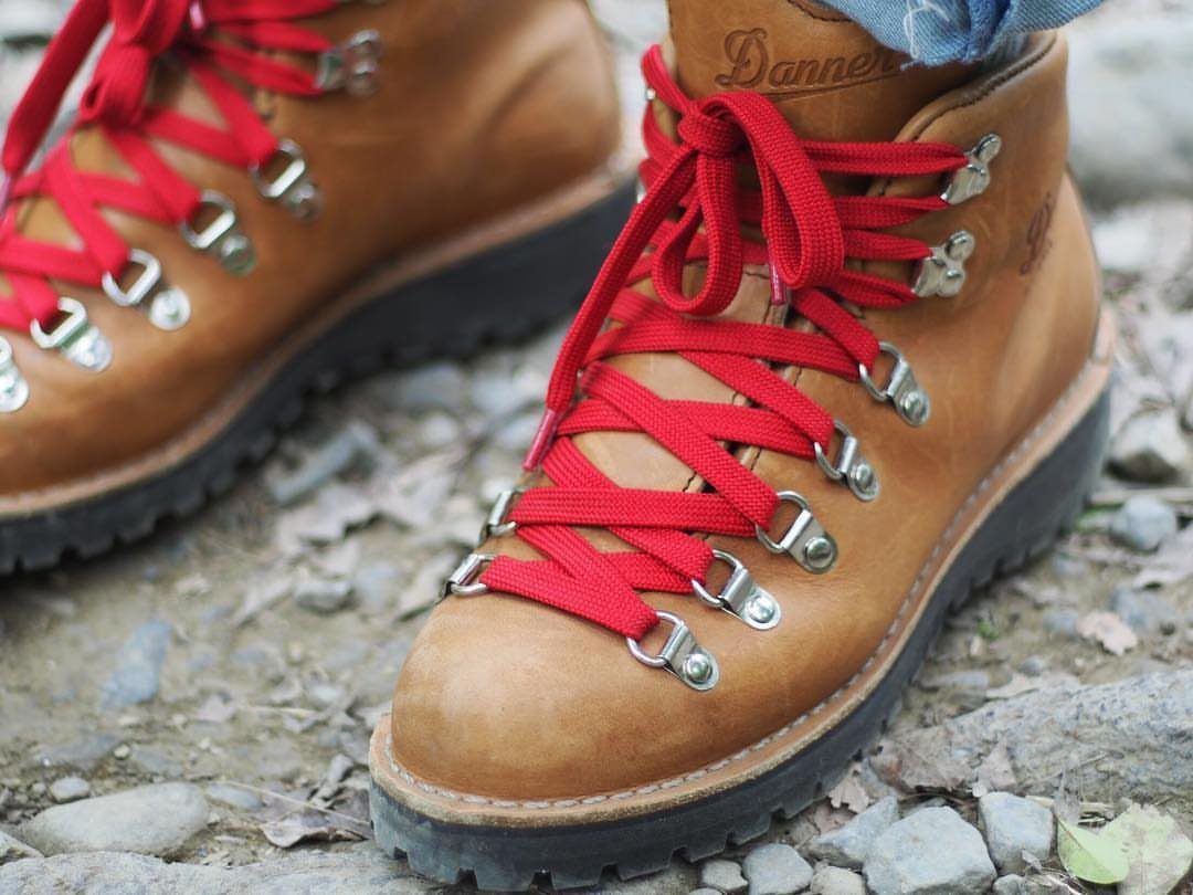 Tan leather Danner Mountain Light boots with red laces on rocky ground.