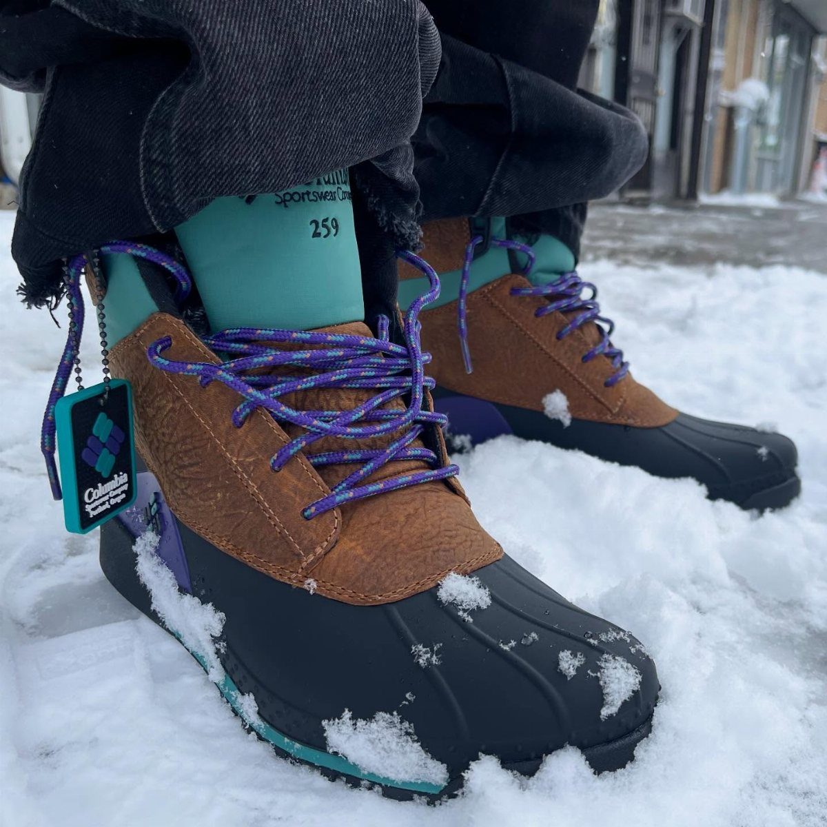 Brown leather and black rubber winter boots with purple laces standing in white snow