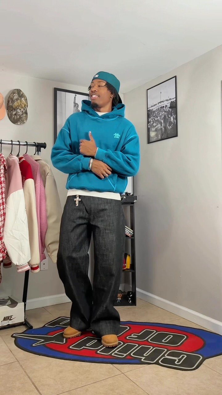 Black man wearing a bright blue hoodie, blue cap, and wide-leg dark jeans.