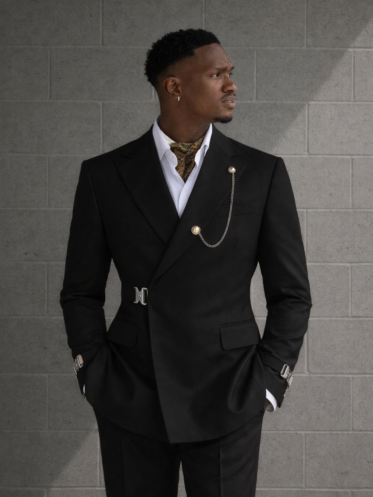 Black man in a tailored black double-breasted suit with a gold cravat and chain.