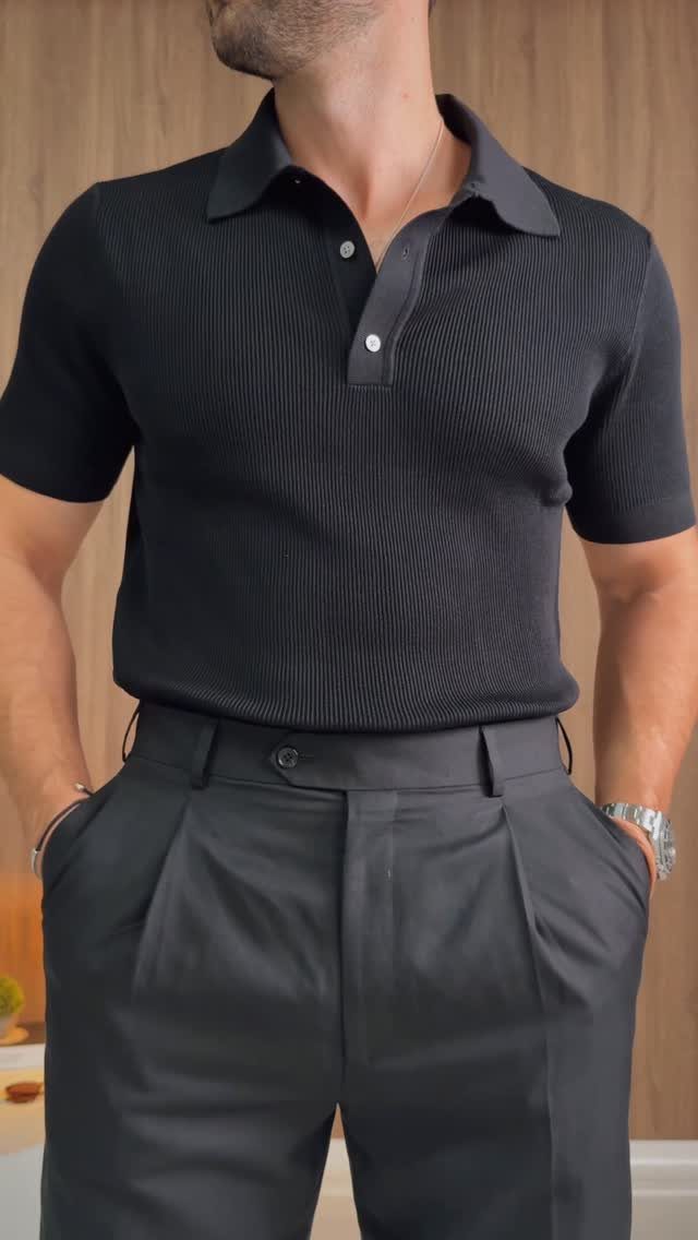 Man wearing a black knit polo shirt and dark grey pleated trousers.