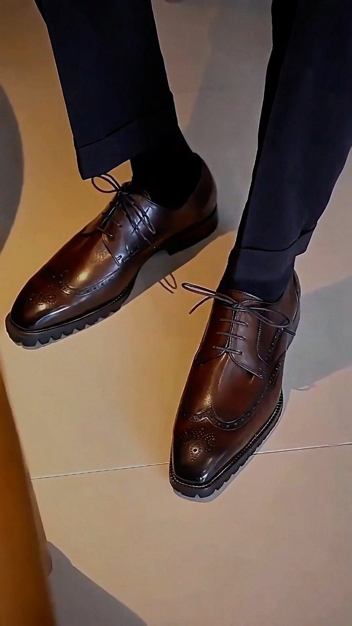 Brown leather brogue shoes paired with dark navy trousers on a light floor.
