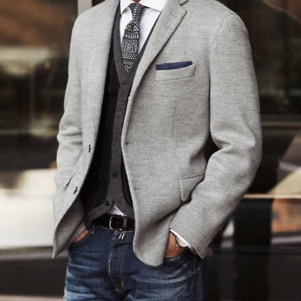Man wearing a light grey unstructured blazer with a cardigan and blue jeans.