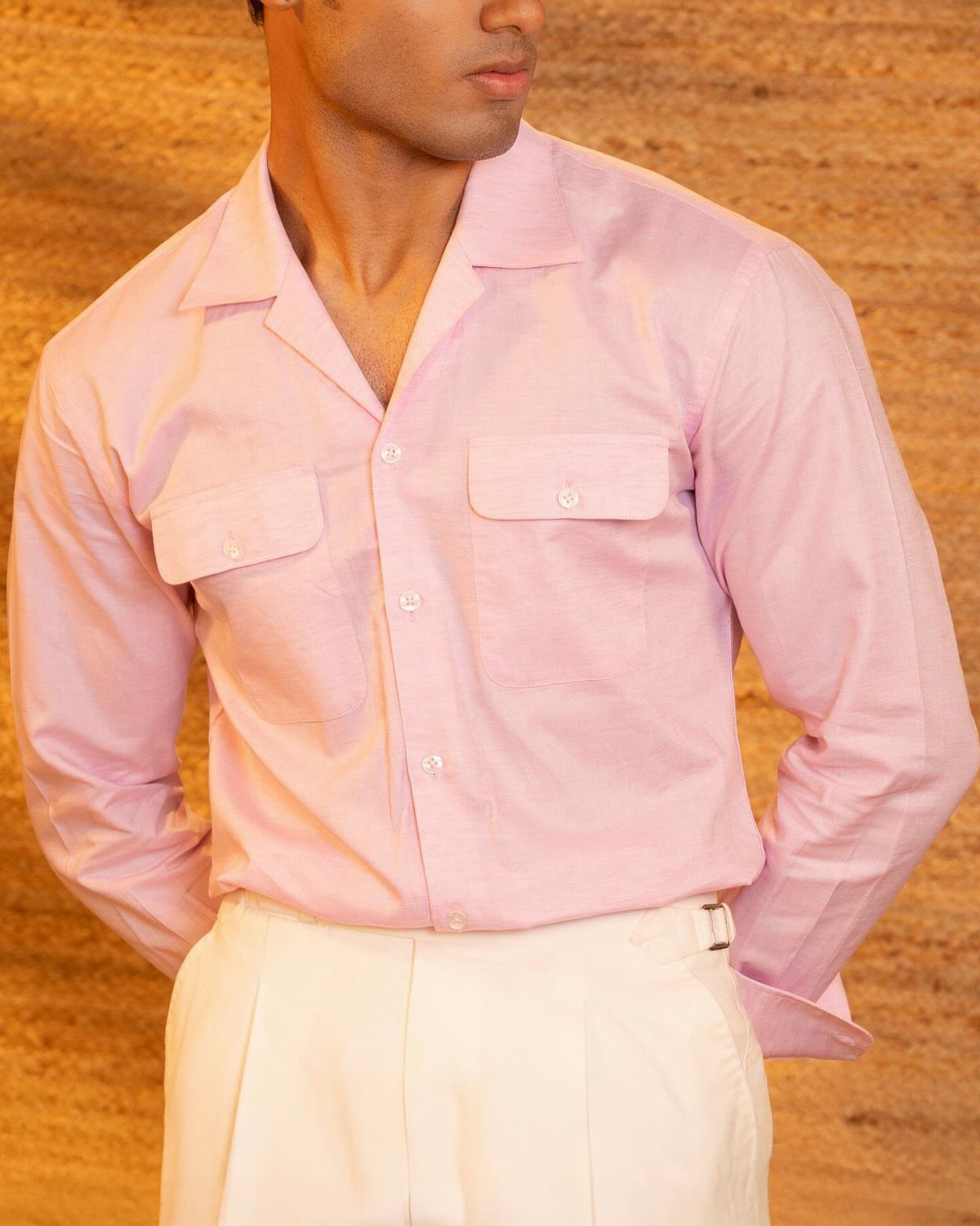 Man wearing a pink camp collar shirt and white trousers against brown background