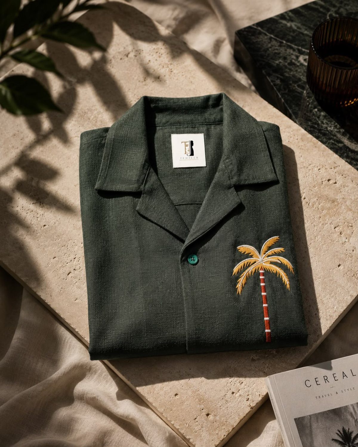 Dark green short-sleeve shirt with an embroidered yellow palm tree on a stone slab