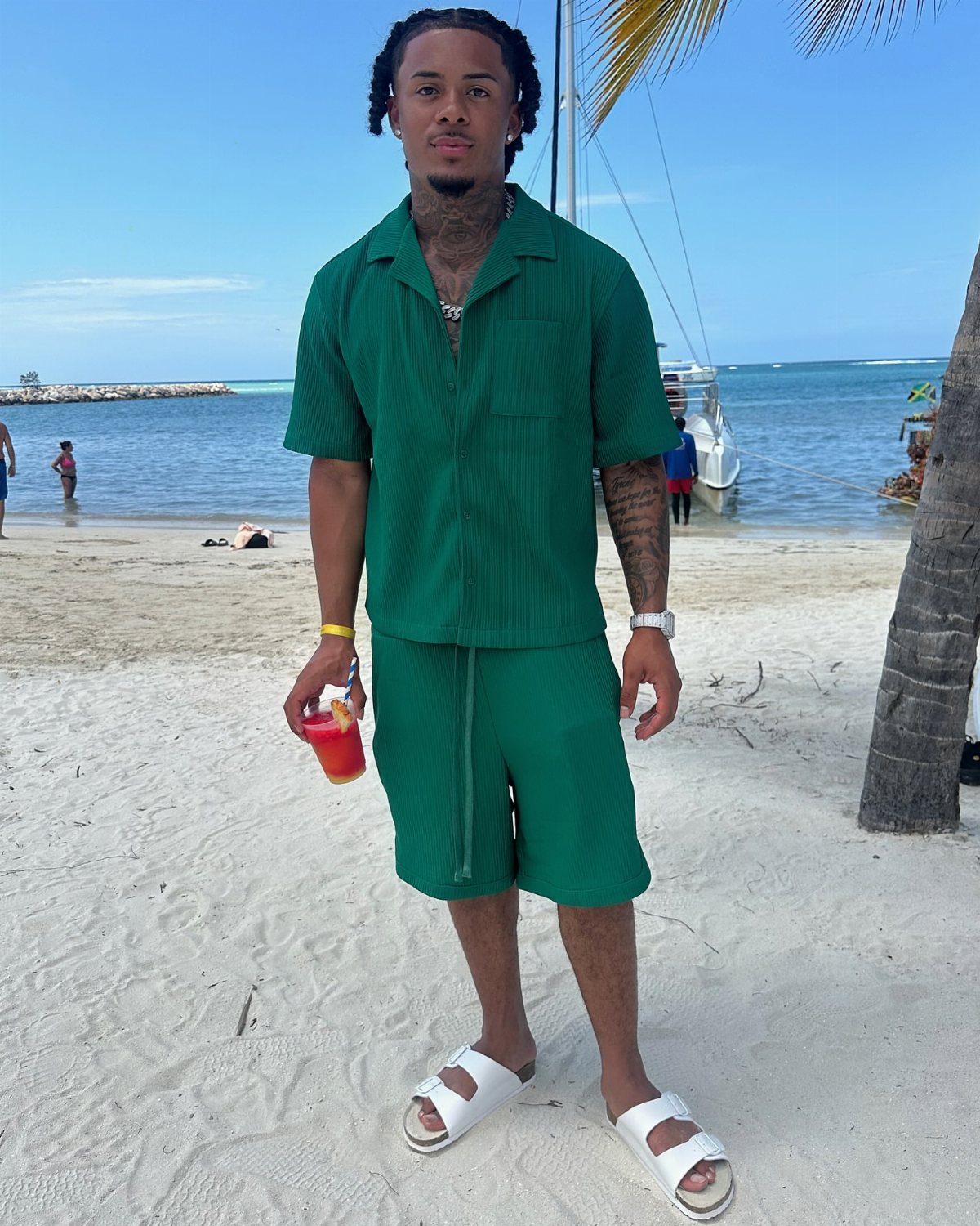 Man in a matching green short-sleeved shirt and shorts set on a beach.