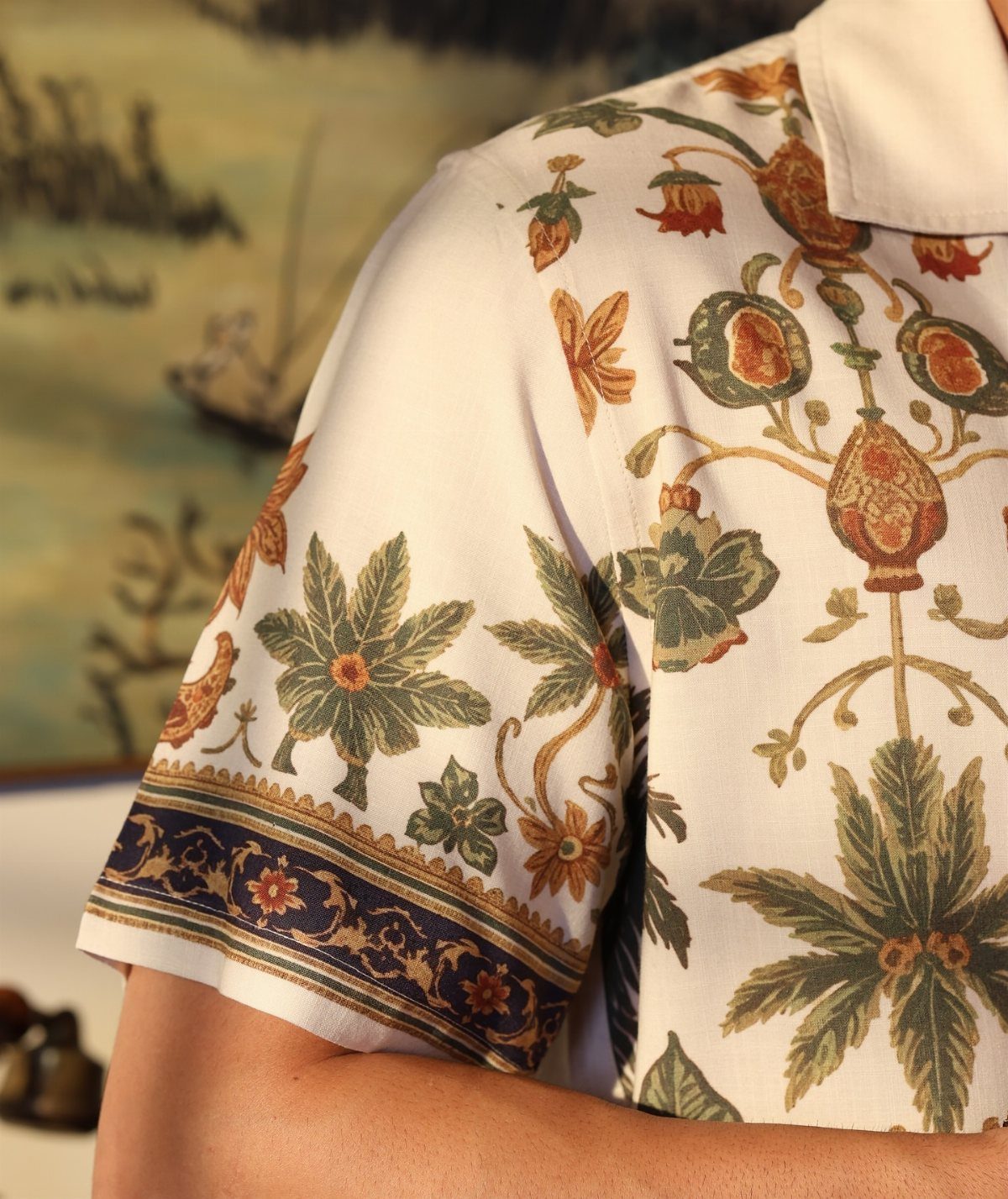 White short-sleeved button-down shirt with tropical floral patterns and a decorative blue border.