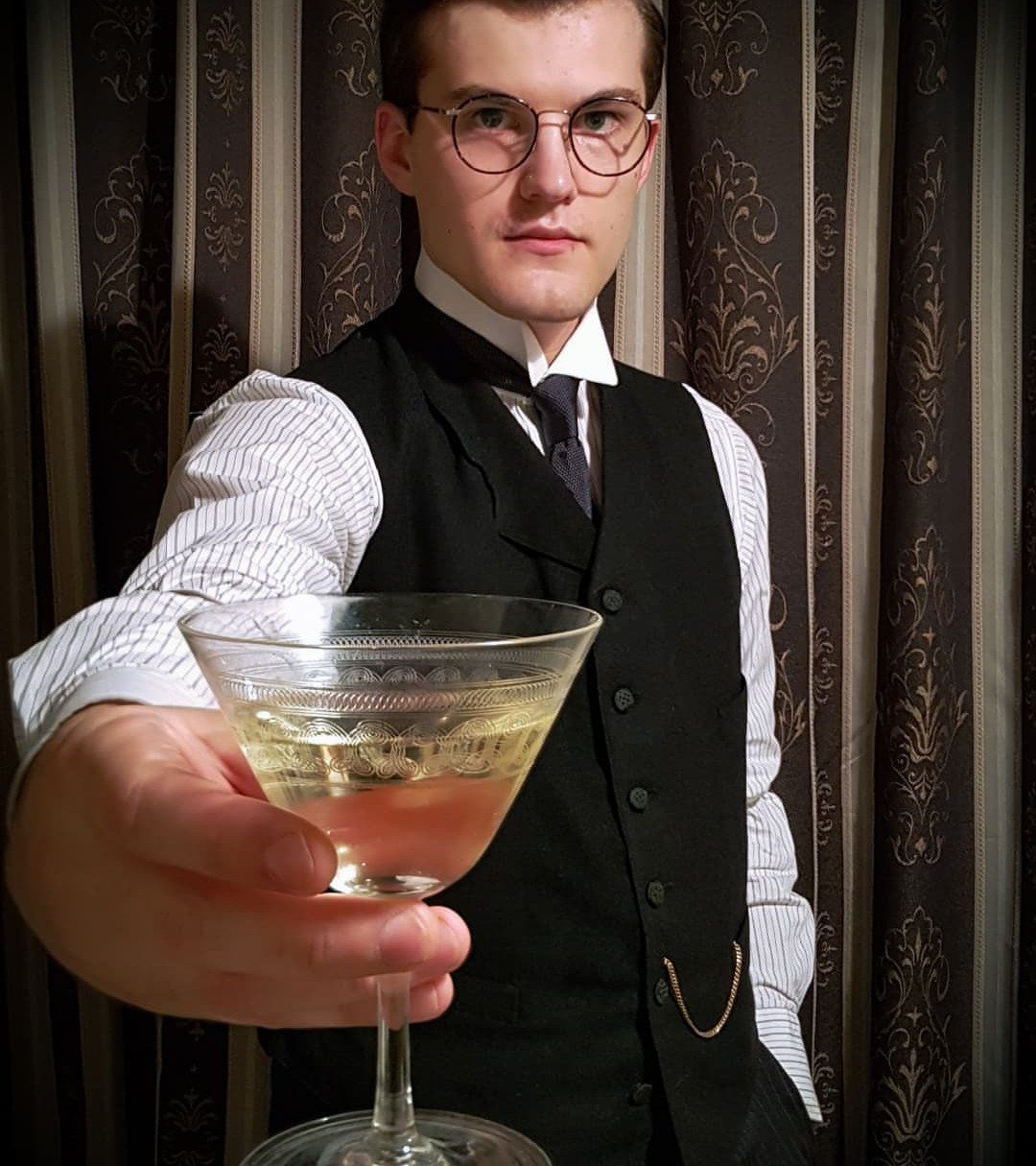 Man in 1900s style waistcoat and high collar holding a cocktail glass.