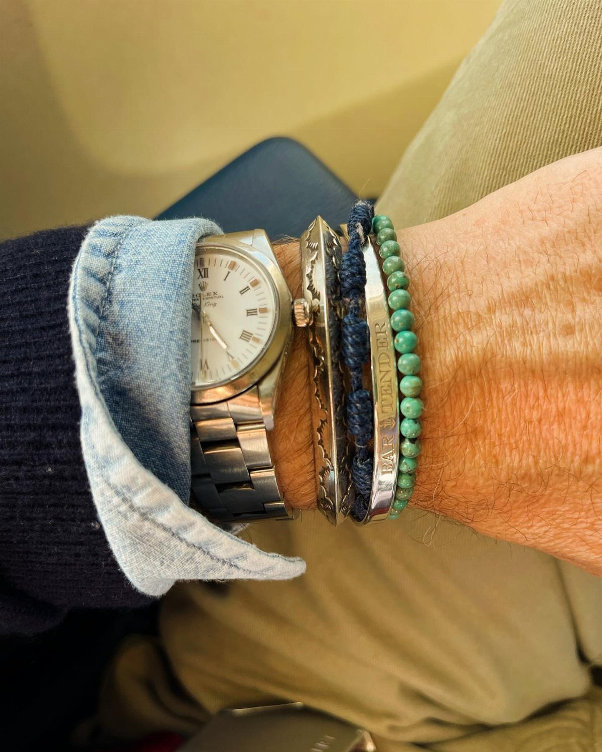 Casual Chic Dress Code Men: 16 Looks That Work in 2026 5 Man's wrist with a silver watch and multiple bracelets, wearing denim and khaki.