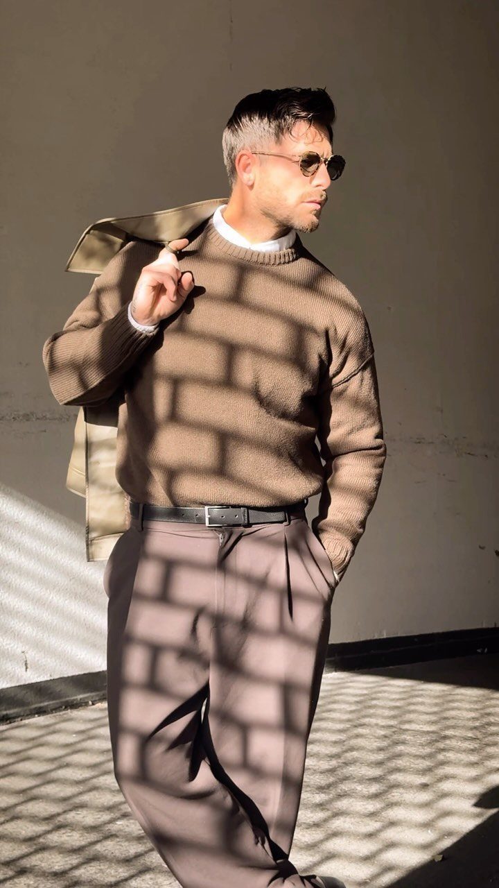 Casual Chic Dress Code Men: 16 Looks That Work in 2026 2 Man in brown sweater and trousers posing with a beige coat over his shoulder.