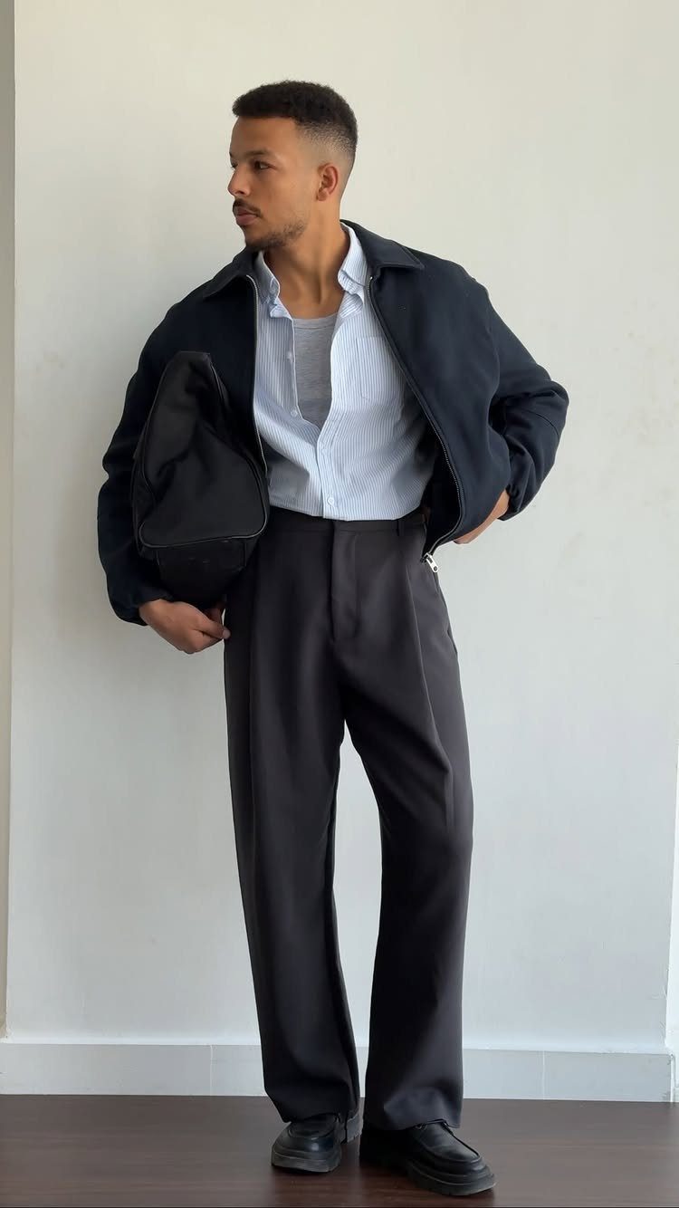 Casual Chic Dress Code Men: 16 Looks That Work in 2026 8 Man in navy jacket, striped shirt, and wide-leg grey trousers posing against white wall.