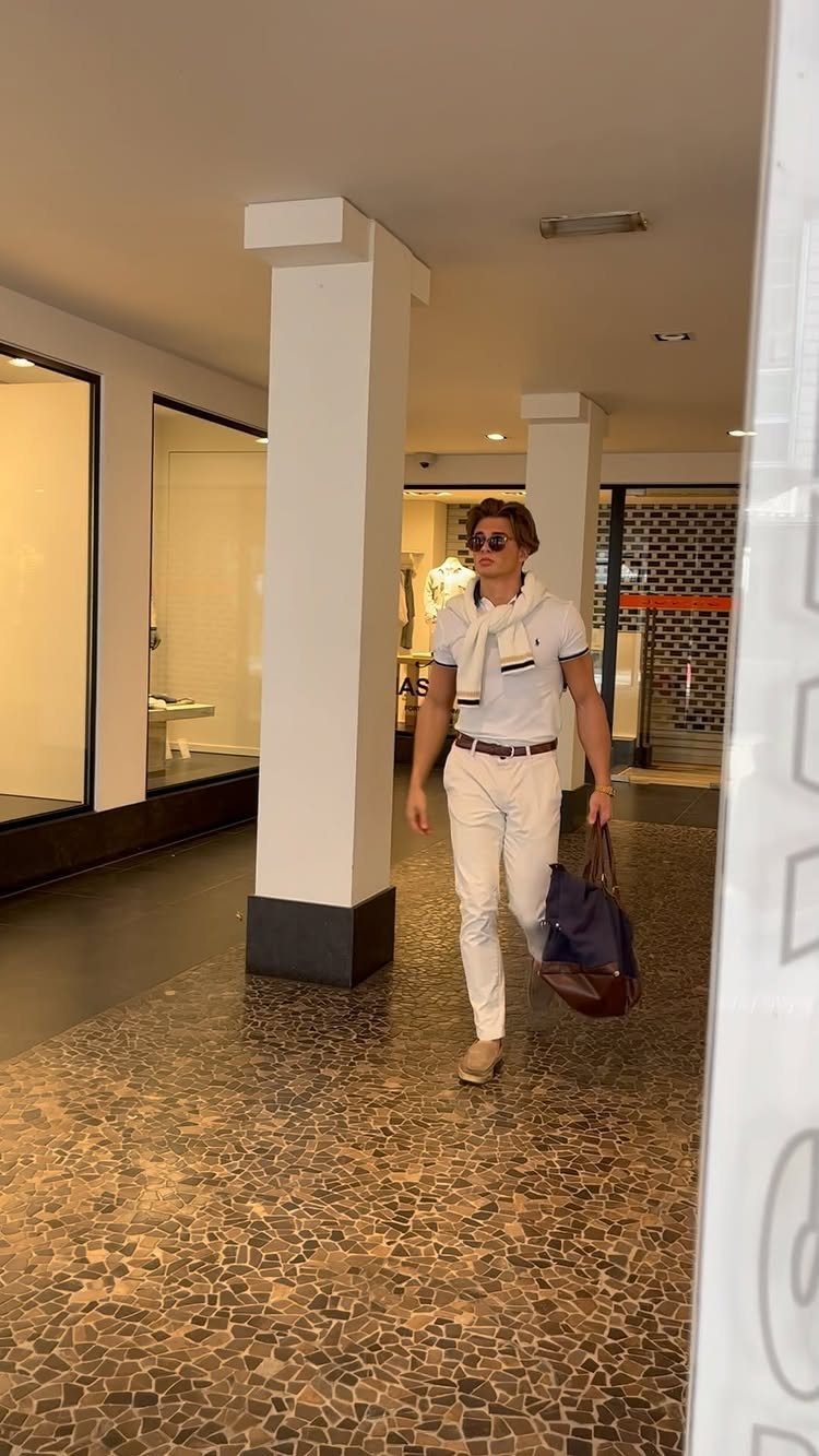 Casual Chic Dress Code Men: 16 Looks That Work in 2026 14 Man in white shirt and trousers with sweater over shoulders carrying a blue bag