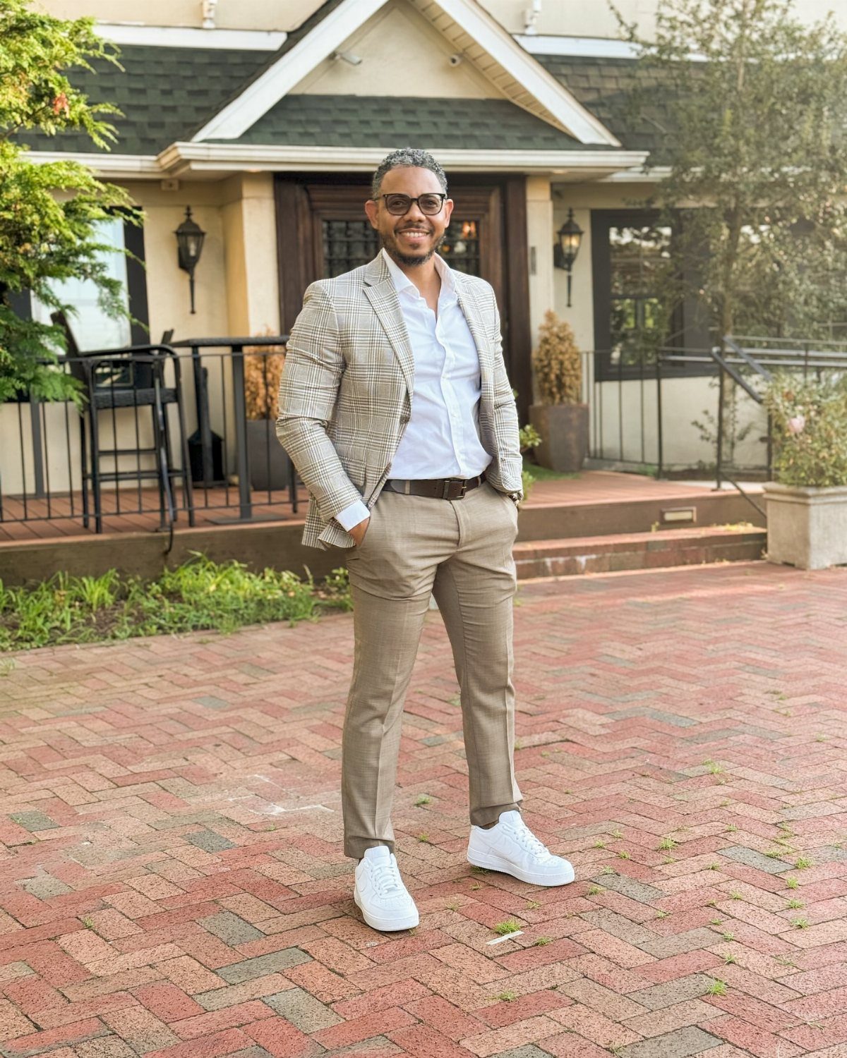 Man in a patterned blazer and tan trousers wearing white sneakers on brick patio