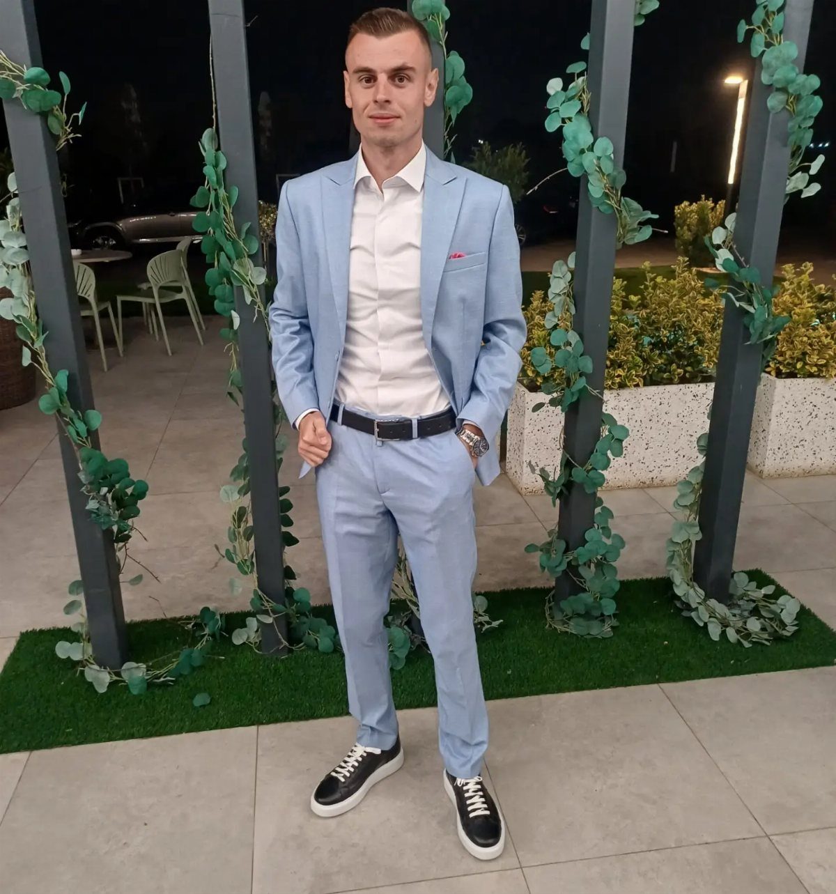 Man in a light blue suit and black sneakers posing outdoors at night.