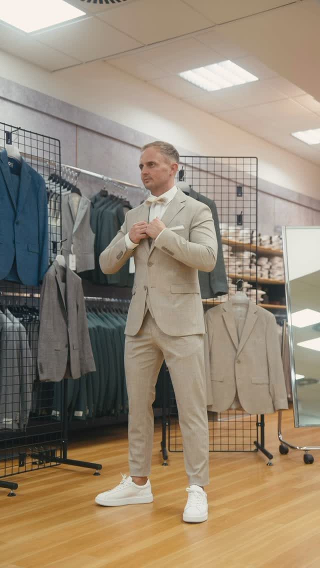 Man in a light beige suit and white sneakers posing in a clothing store.