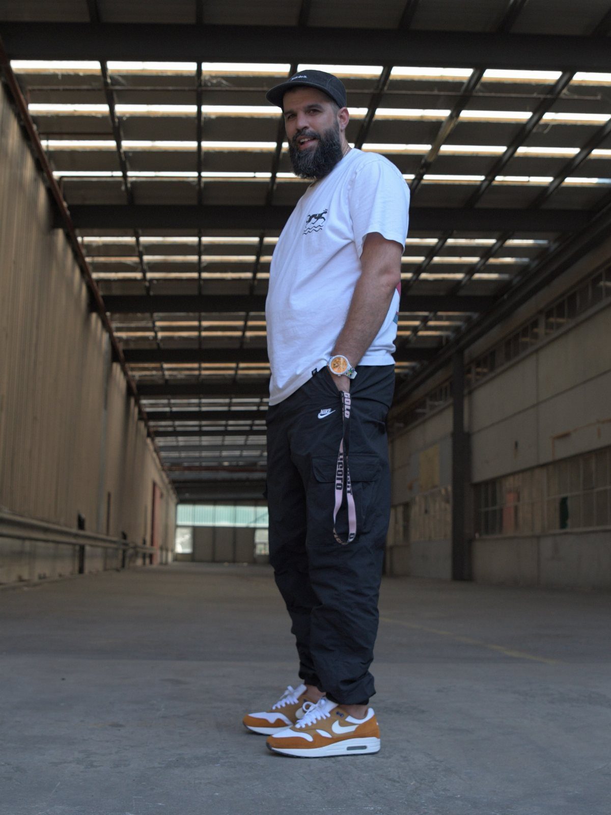 Man in white t-shirt, black cargo pants, and orange sneakers in industrial warehouse.