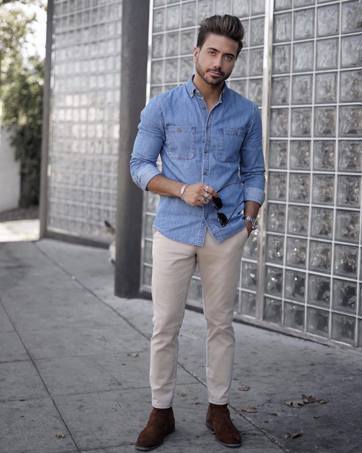 Man wearing a blue denim shirt, beige chinos, and brown suede boots outdoors.
