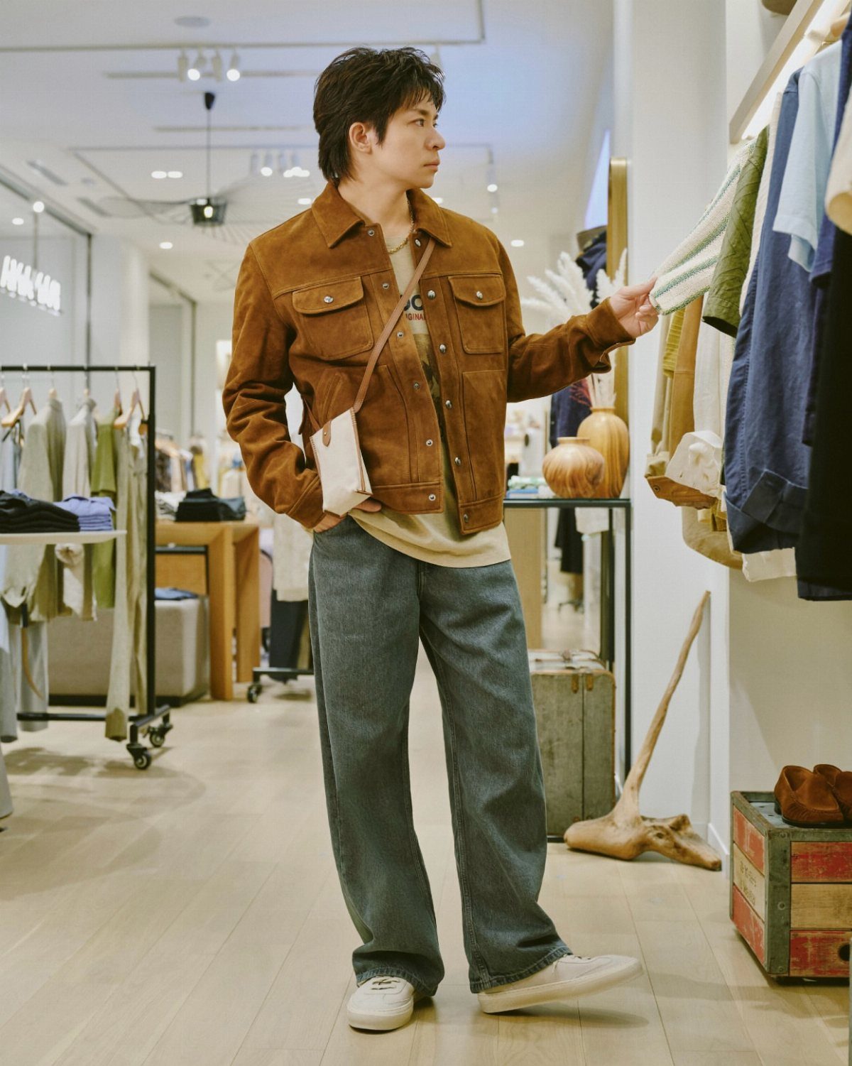 Man wearing a brown suede jacket and wide jeans browsing clothes in a store