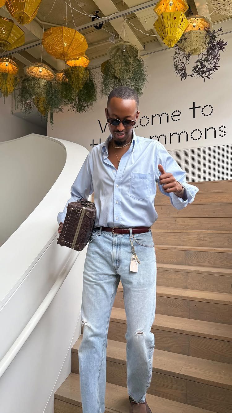 Man in light blue shirt and distressed jeans holding a leather briefcase on stairs.