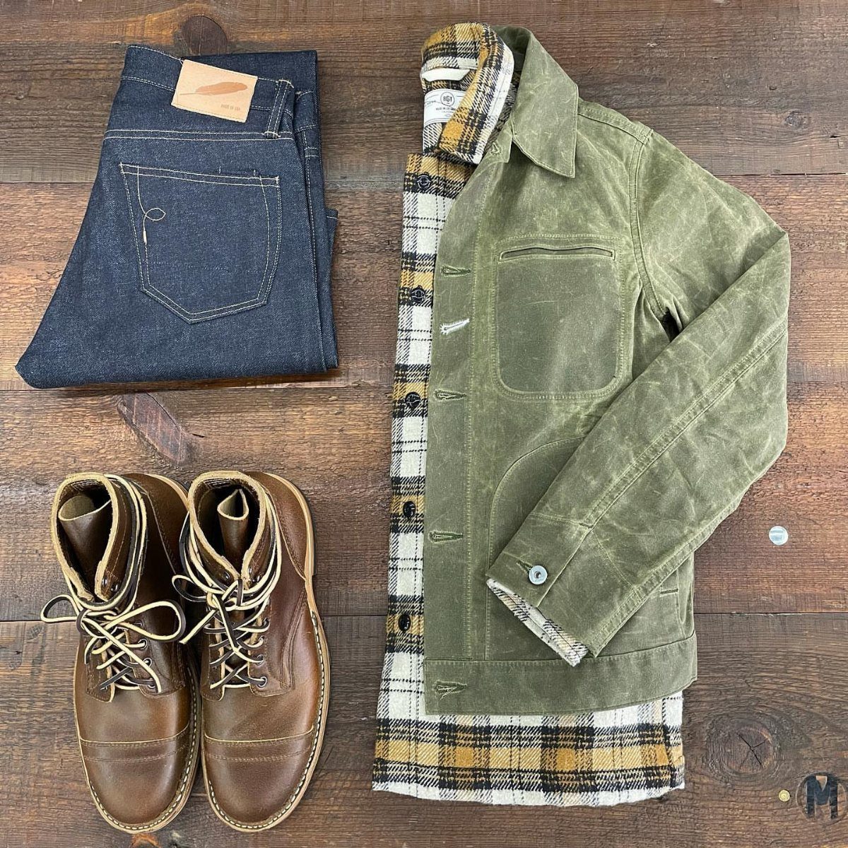 Dark blue denim jeans, olive green jacket, plaid shirt, and brown leather boots.