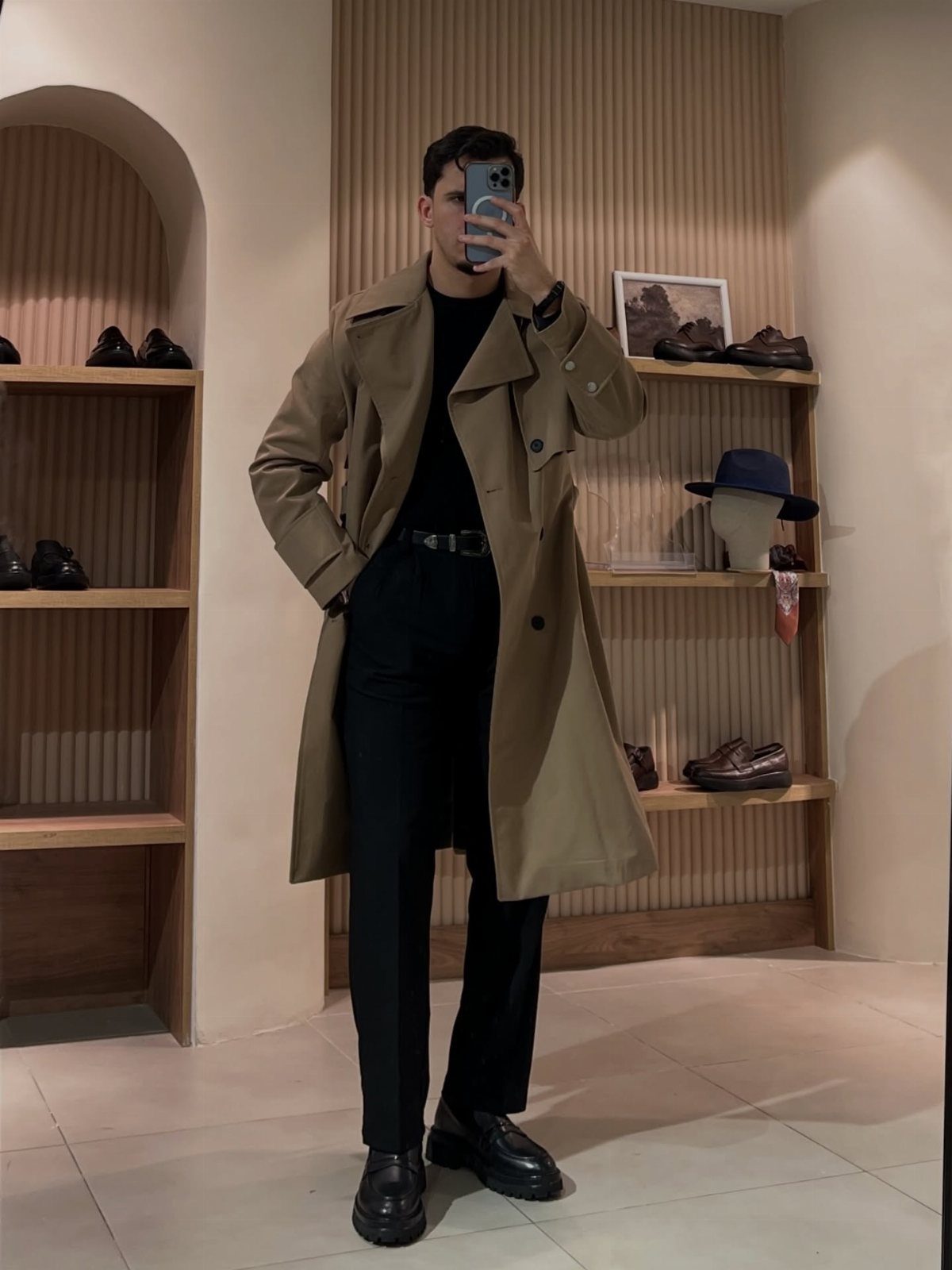 Man wearing a tan trench coat and black outfit in a shoe store.