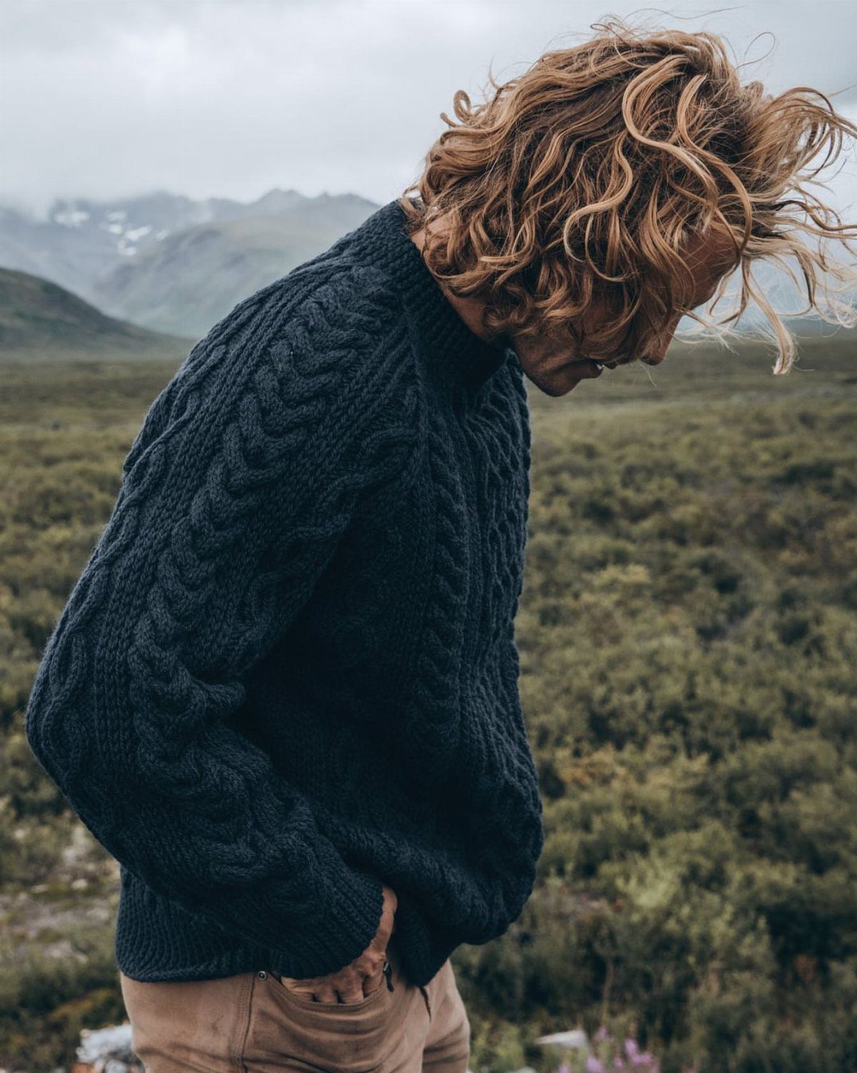 Man wearing a navy blue cable-knit fisherman sweater in a green hilly landscape.