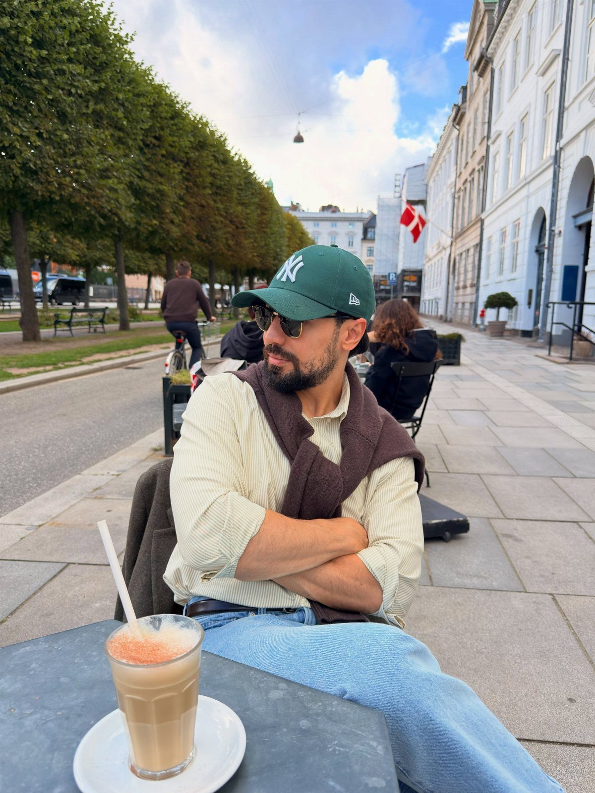 Man in a green cap and layered clothing sitting at a Copenhagen cafe.