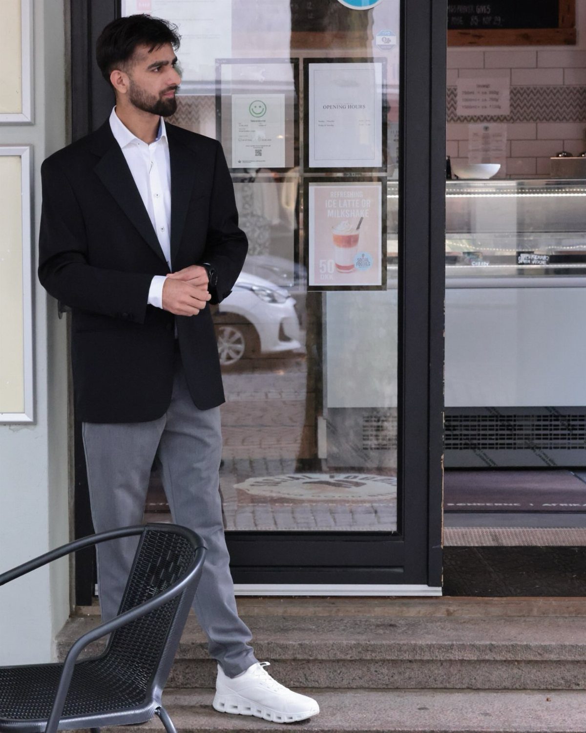 Man in black blazer and grey trousers standing outside a cafe.