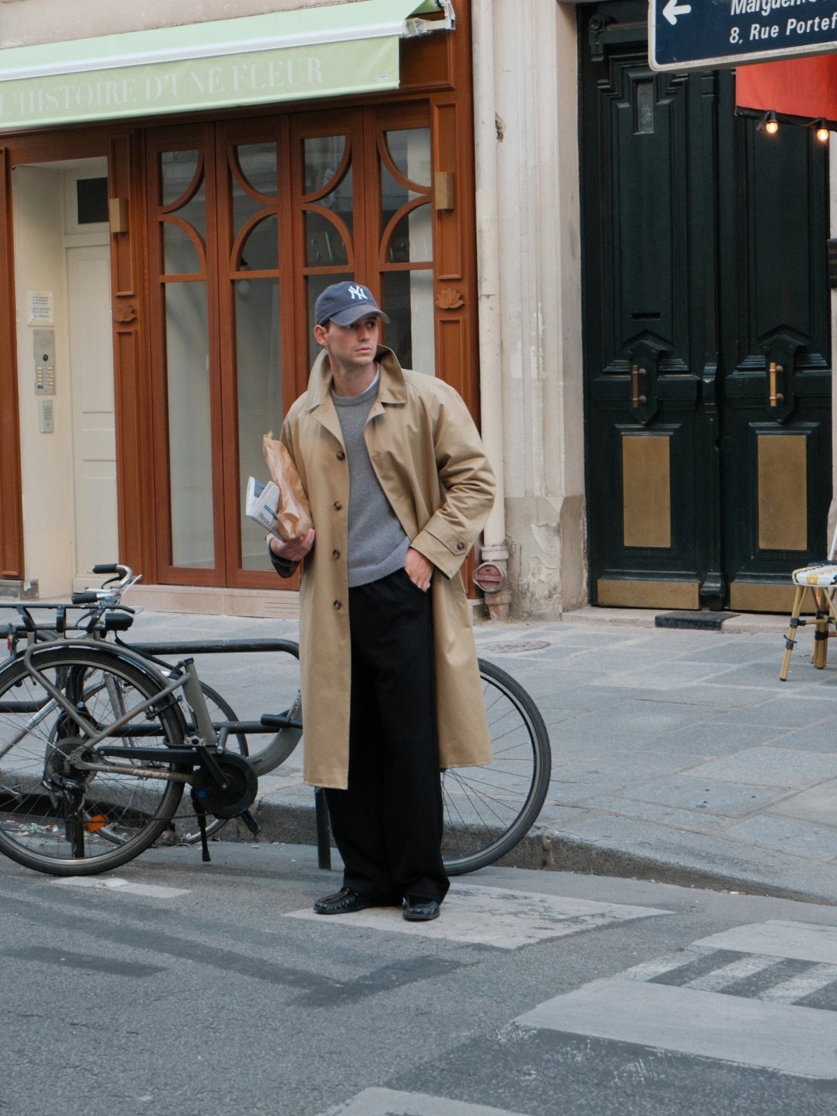 Man in tan trench coat and blue cap standing on a city street.