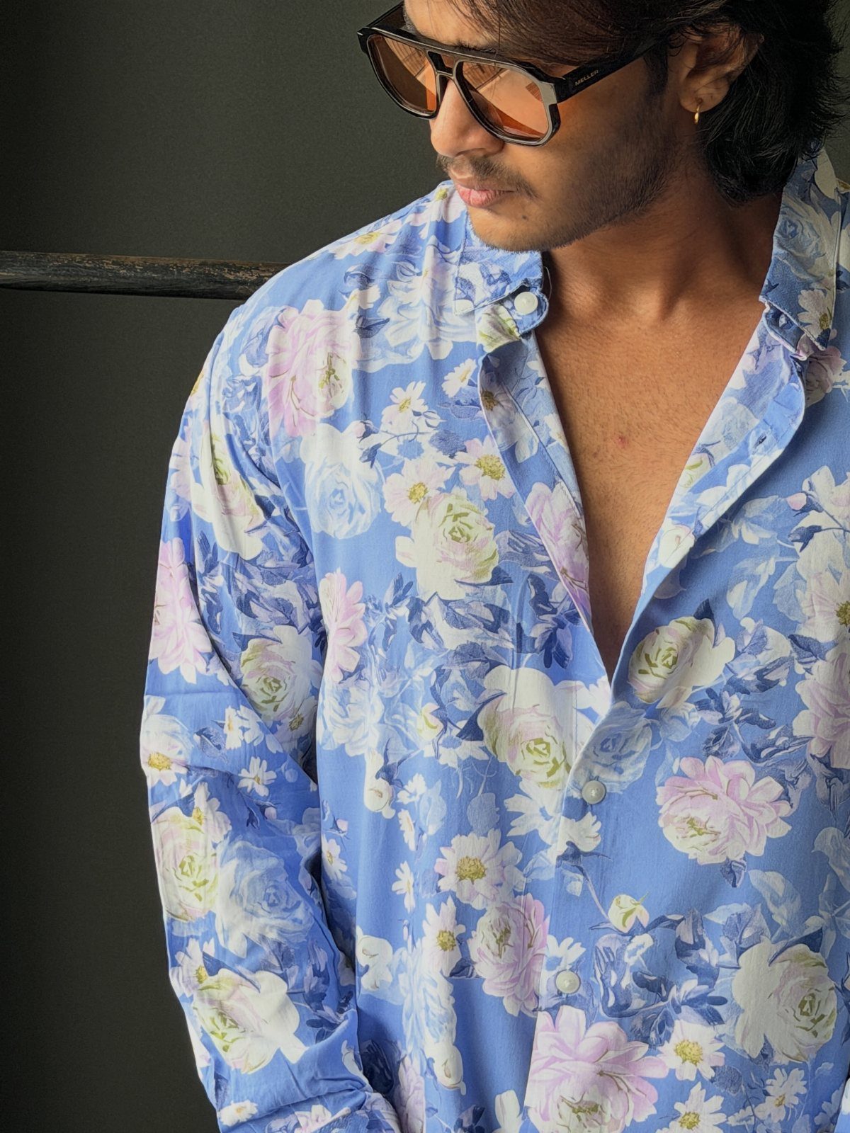 Man wearing a blue button-down shirt with bold, colorful floral prints and sunglasses.