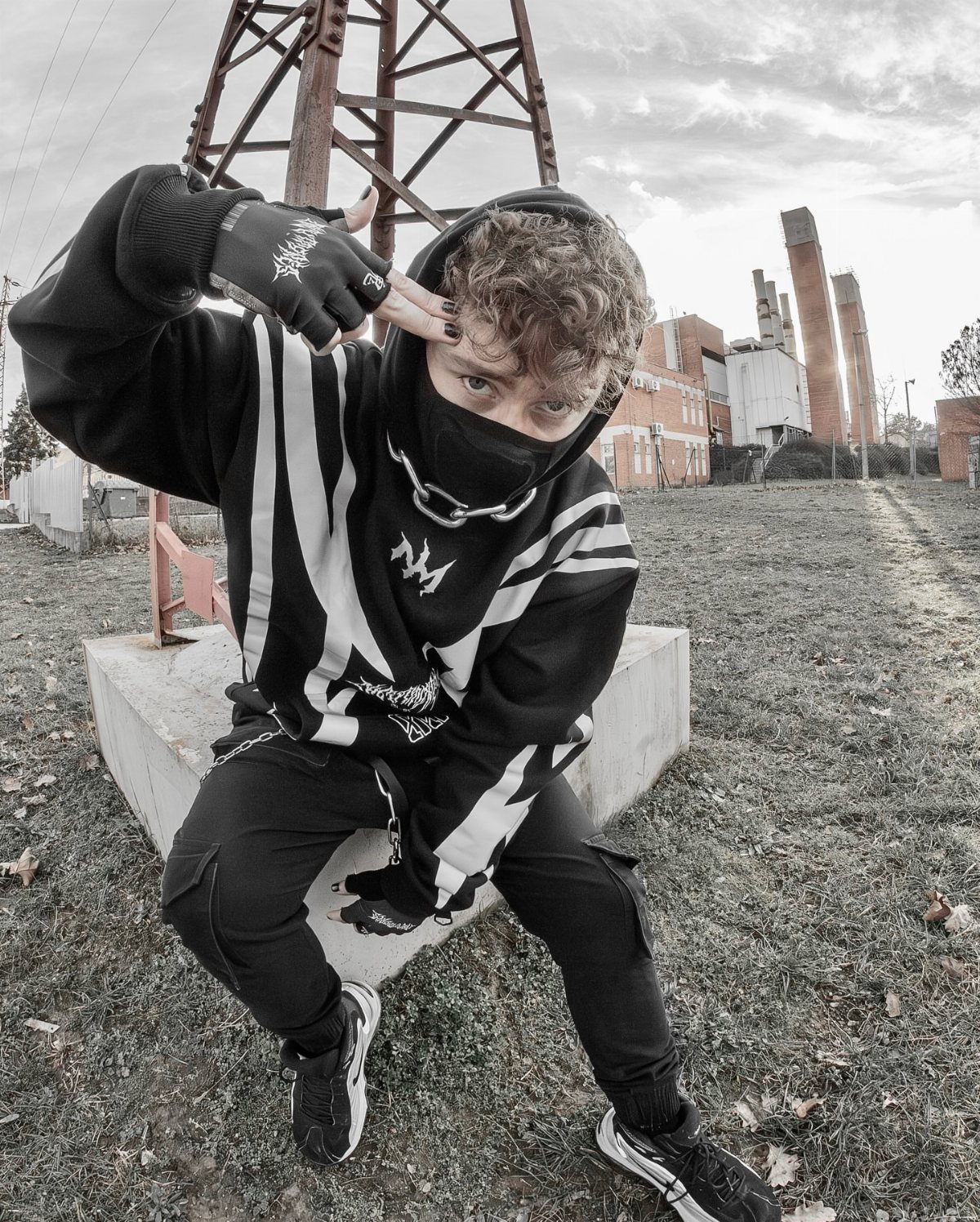 Young man in a black and white oversized hoodie and face mask posing outdoors.
