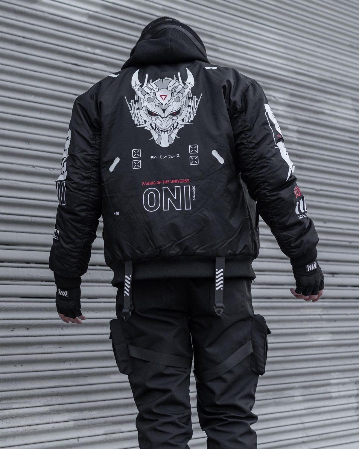 Man from behind wearing a black cyberpunk bomber jacket and black cargo pants.