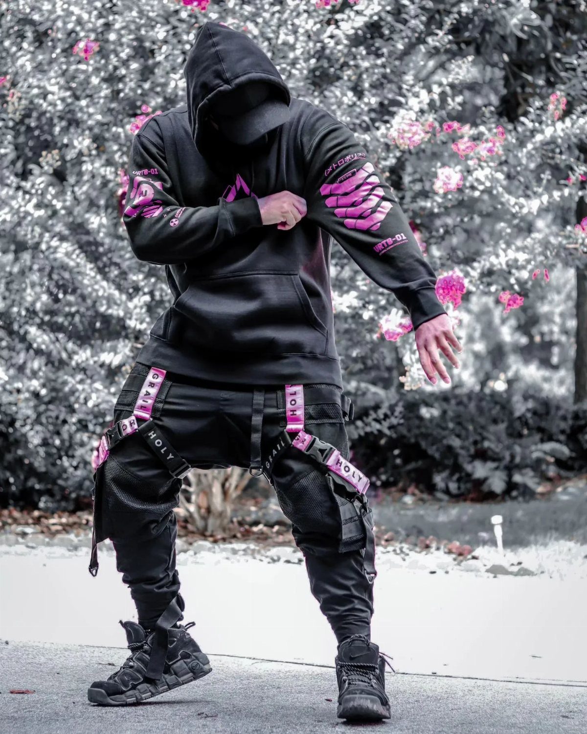 Man in black cyberpunk streetwear with pink skeletal prints and strapped cargo pants.