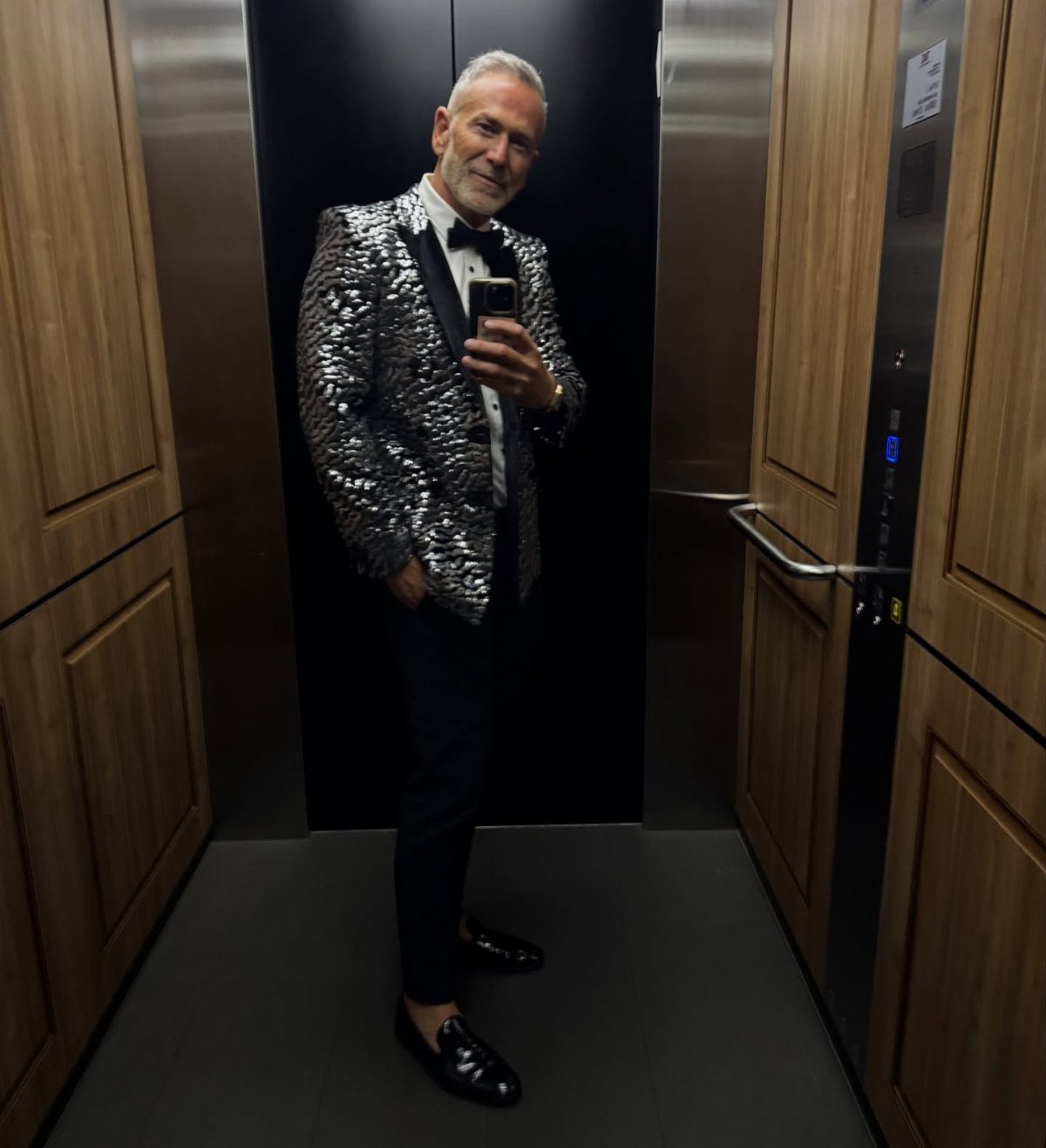 Man in a silver sequined blazer and bow tie posing in an elevator
