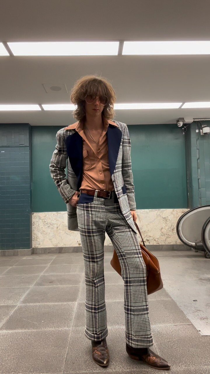 Man in a vintage plaid suit and orange shirt posing in a hallway.