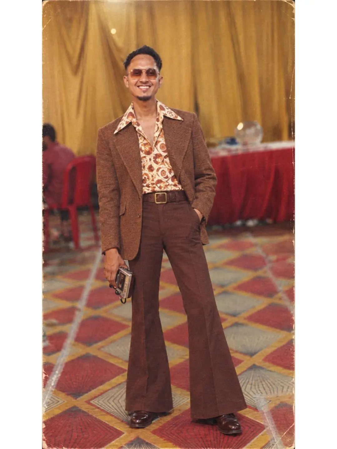 Man in 70s disco fashion wearing a wide-collar patterned shirt and bell-bottoms.
