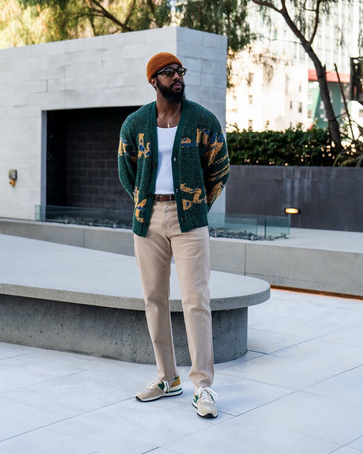 Man wearing a green patterned knit cardigan, beige trousers, and a brown beanie.