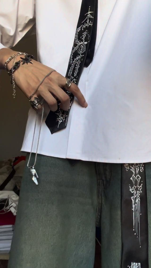 Person wearing silver gothic rings, bracelets, and a long chain necklace with a pendant.